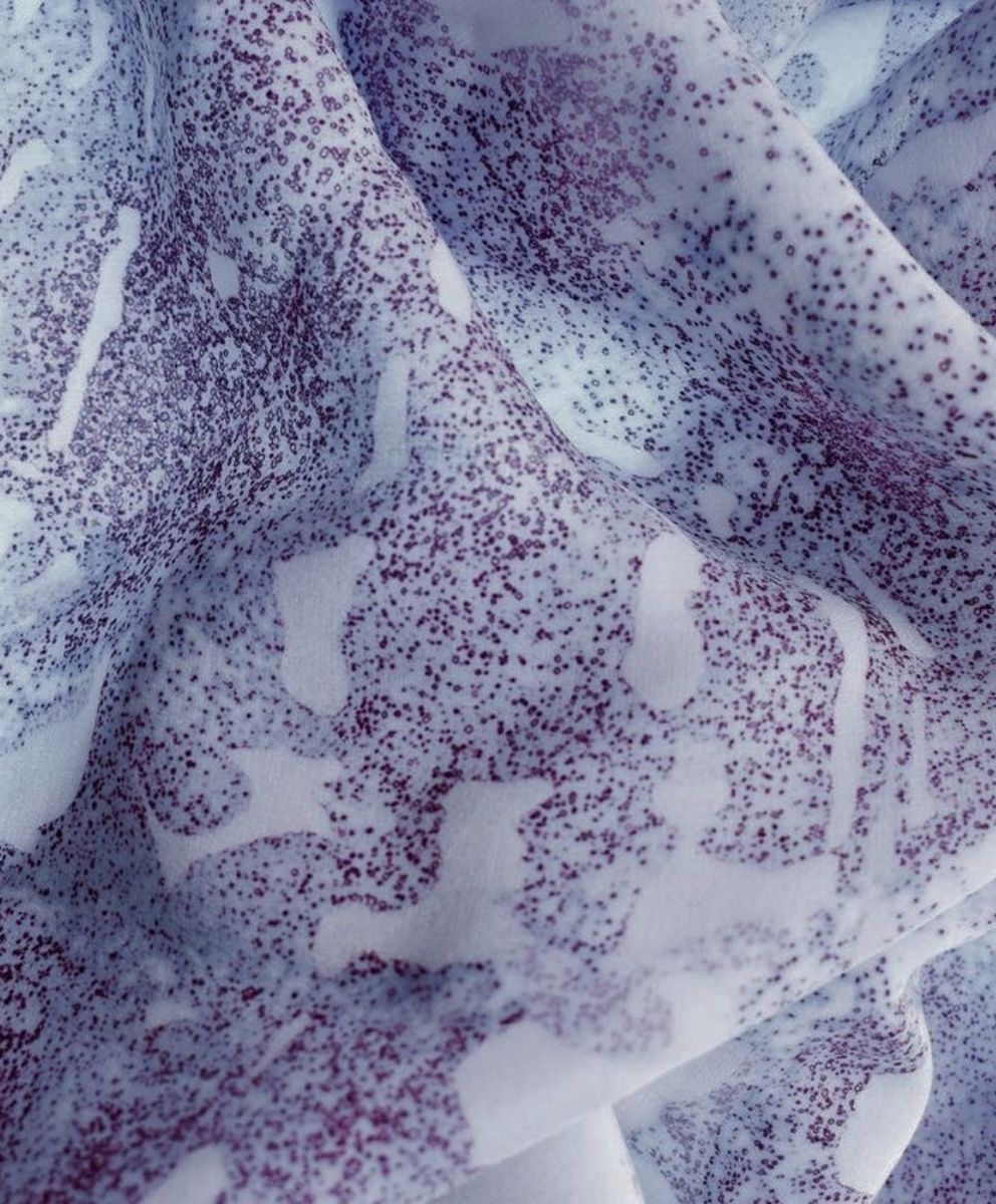Close-up of eco-conscious fabric featuring abstract purple micro-patterns on a soft white base – representing sustainable textile innovation.