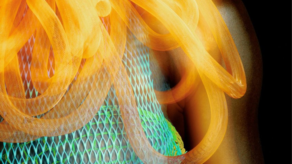 Close-up of a futuristic fashion design featuring neon orange tubing over a green and cyan mesh garment, symbolizing AI-enhanced creativity and digital identity.
