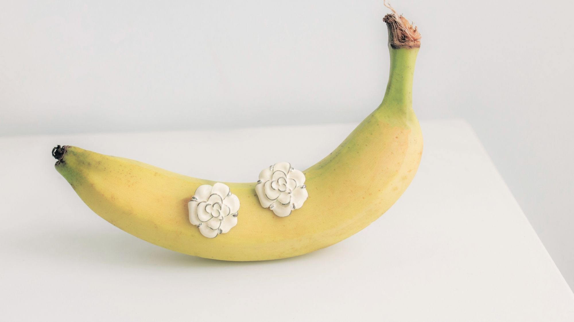 Yellow banana adorned with white floral earrings, styled by C2 Fashion Studio as surreal fashion symbolism.