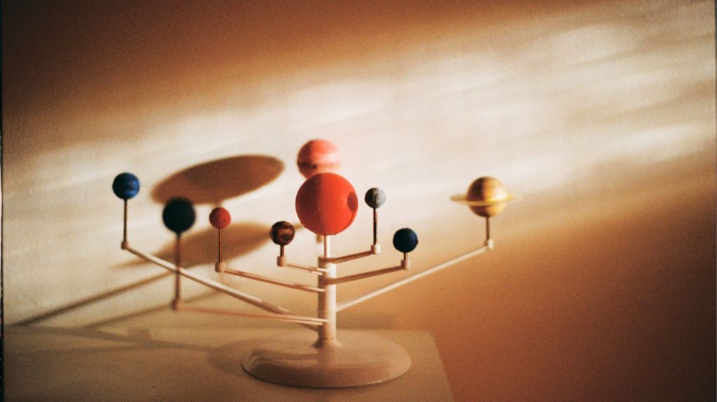 Solar system model under warm light, symbolizing cosmic systems and regenerative trend forecasting by C2 Fashion Studio.