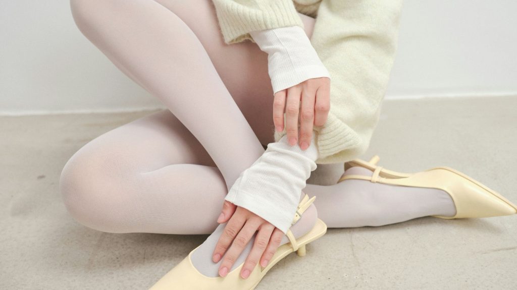 Close-up of layered white knitwear, tights, and pale yellow heels styled by C2 Fashion Studio for the Soft Rebellion trend.