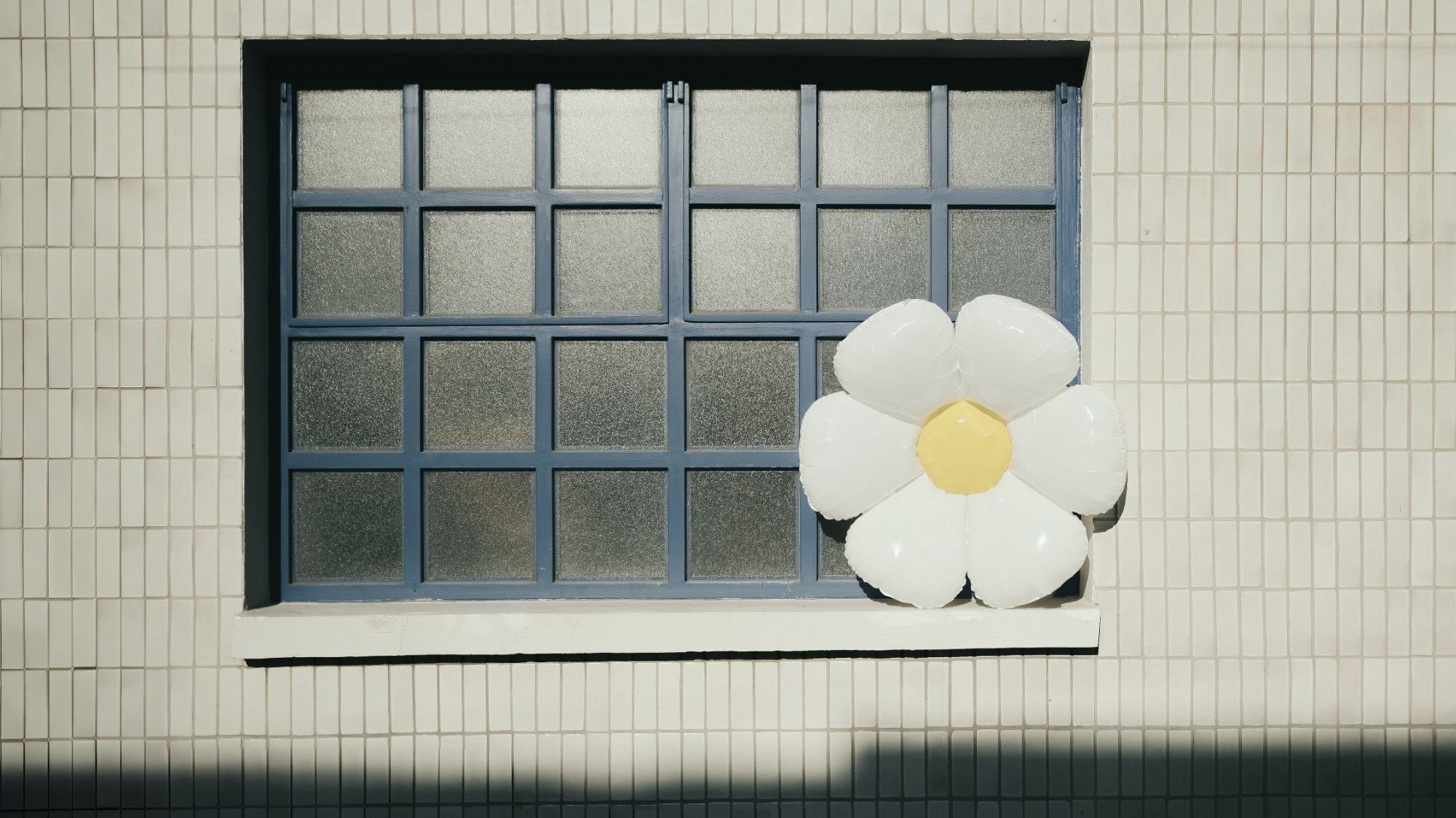 Blue grid window with oversized daisy decor on tiled wall, styled for C2 Fashion Studio’s Soft Rebellion trend.