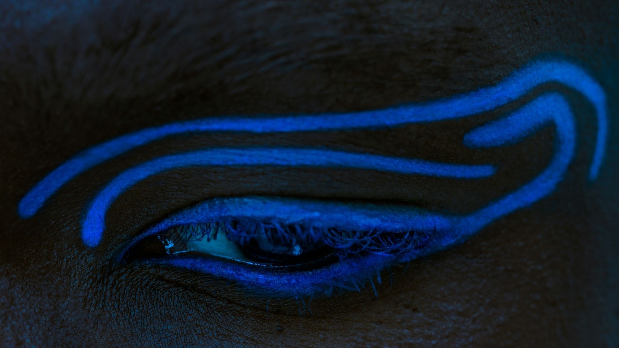 Extreme close-up of a closed eye with glowing blue tribal-style eyeliner, representing futuristic cultural symbolism and identity.