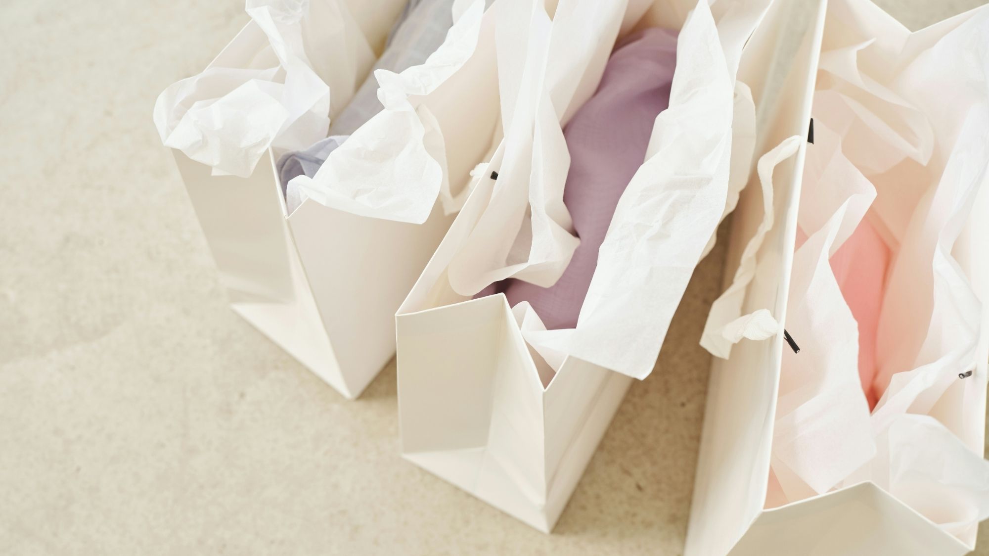Minimal shopping bags with pastel-colored tissue paper, representing conscious consumption and emotional value in fashion trend forecasting.