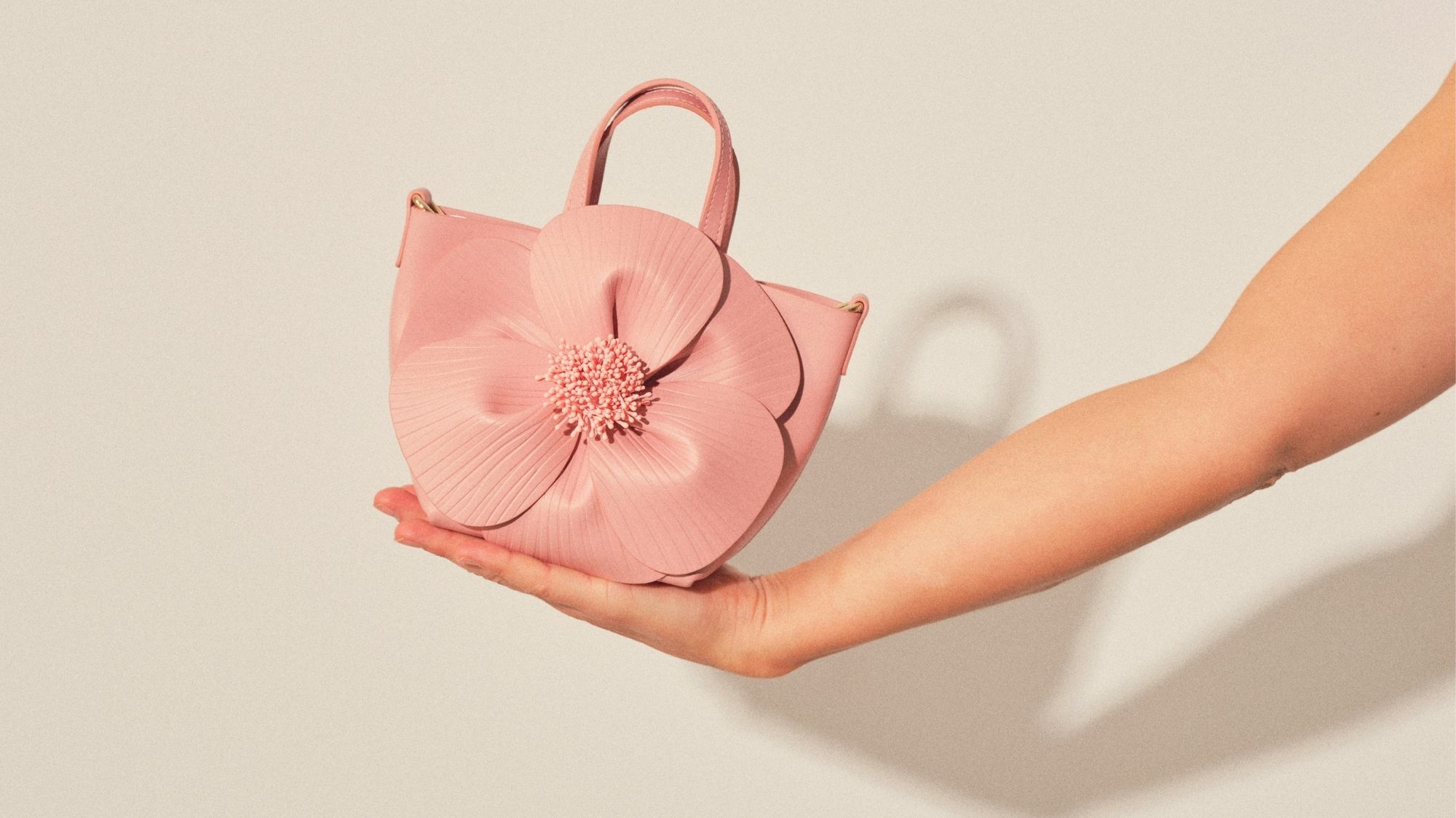 A sculptural pink handbag in the shape of a flower, held by an extended hand, representing emotional durability and fashion trend forecasting insights.