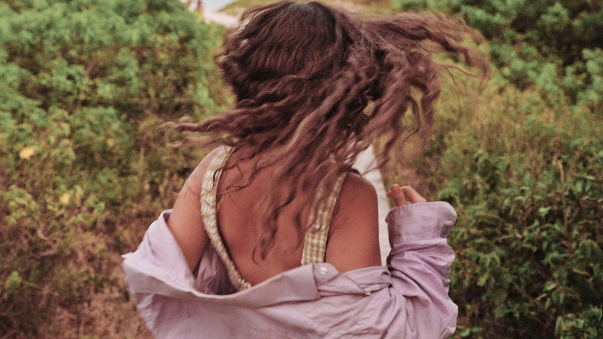 Woman in motion with curly hair, wearing gingham top and lilac shirt — a natural lifestyle moment captured by a trend forecasting tool for influencers and creators.
