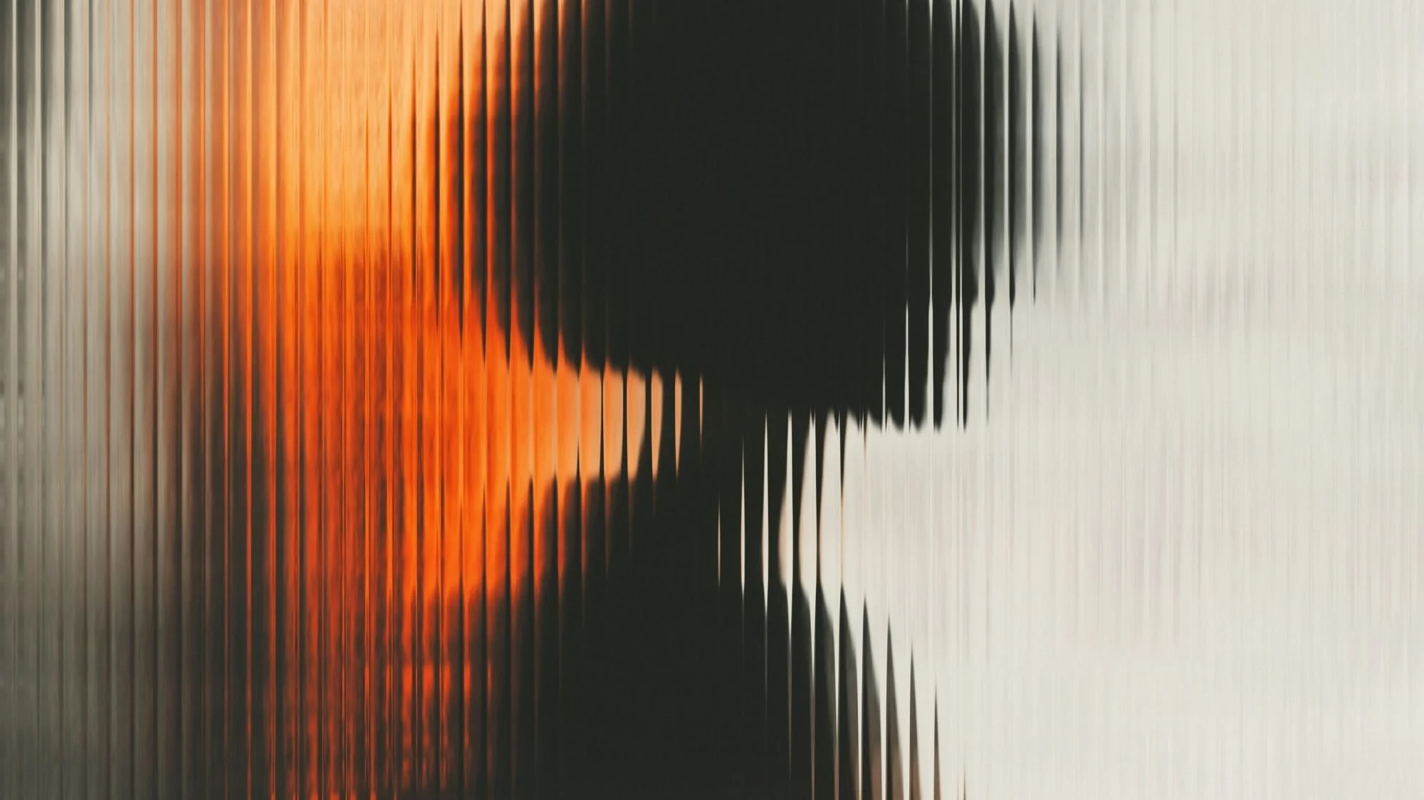 Abstract silhouette behind textured glass with warm orange glow and blurred shadow — symbolizing identity, emotion, and regenerative design futures.