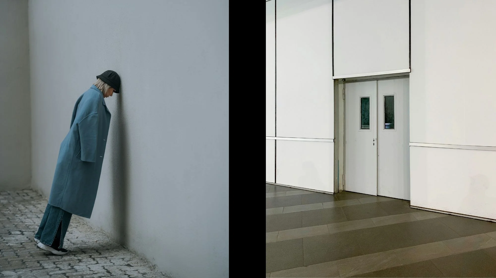 Person in oversized blue coat leaning against a wall beside minimal white industrial door — fashion and architecture in silent dialogue