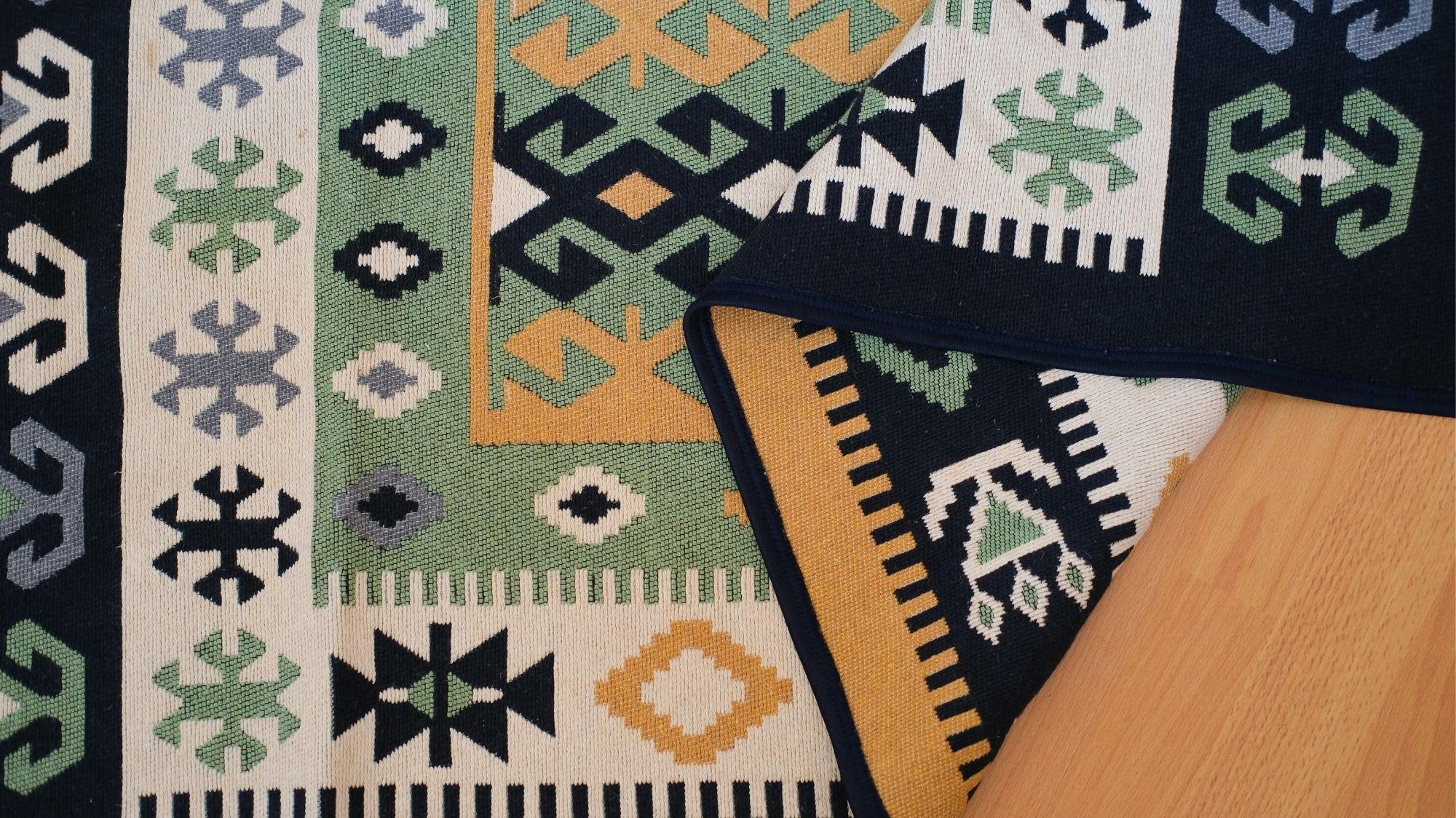 Close-up of a traditional woven textile rug with geometric tribal motifs in green, yellow, black, and grey, reflecting artisan craft and cultural heritage in fashion forecasting by C2 Fashion Studio, a global trend forecasting agency.