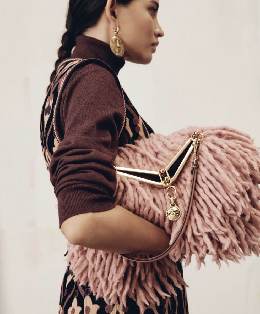 Model carrying a textured pink bohemian-inspired bag with gold hardware and wearing bold artisan earrings, symbolizing cultural nomadism and conscious bohemian aesthetics in trend forecasting for Spring Summer 2027 2028 by C2 Fashion Studio, a global trend forecasting agency.