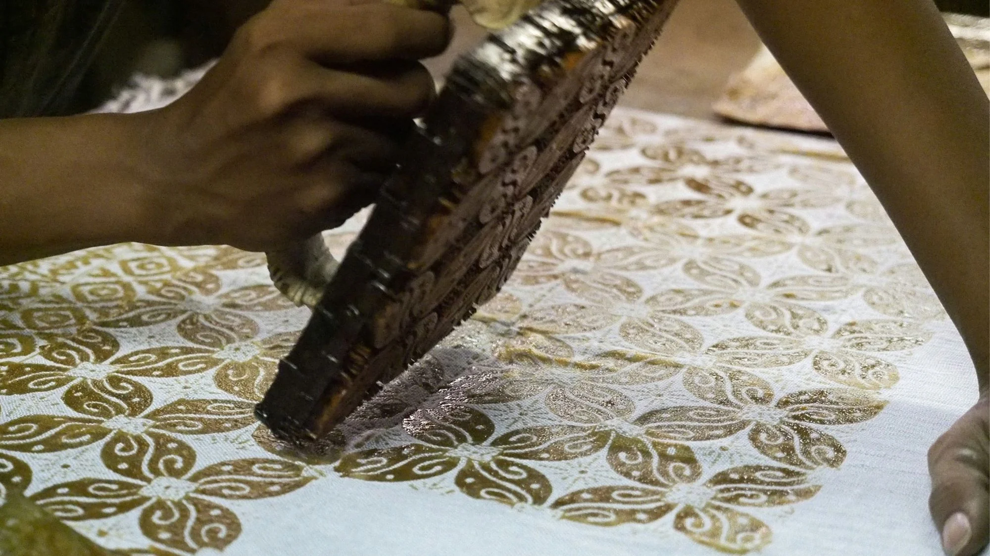 Close-up of artisan hand block-printing golden patterns on fabric, representing craftsmanship and cultural heritage in a fashion trend studied by C2 Fashion Studio, a leading trend forecasting agency.
