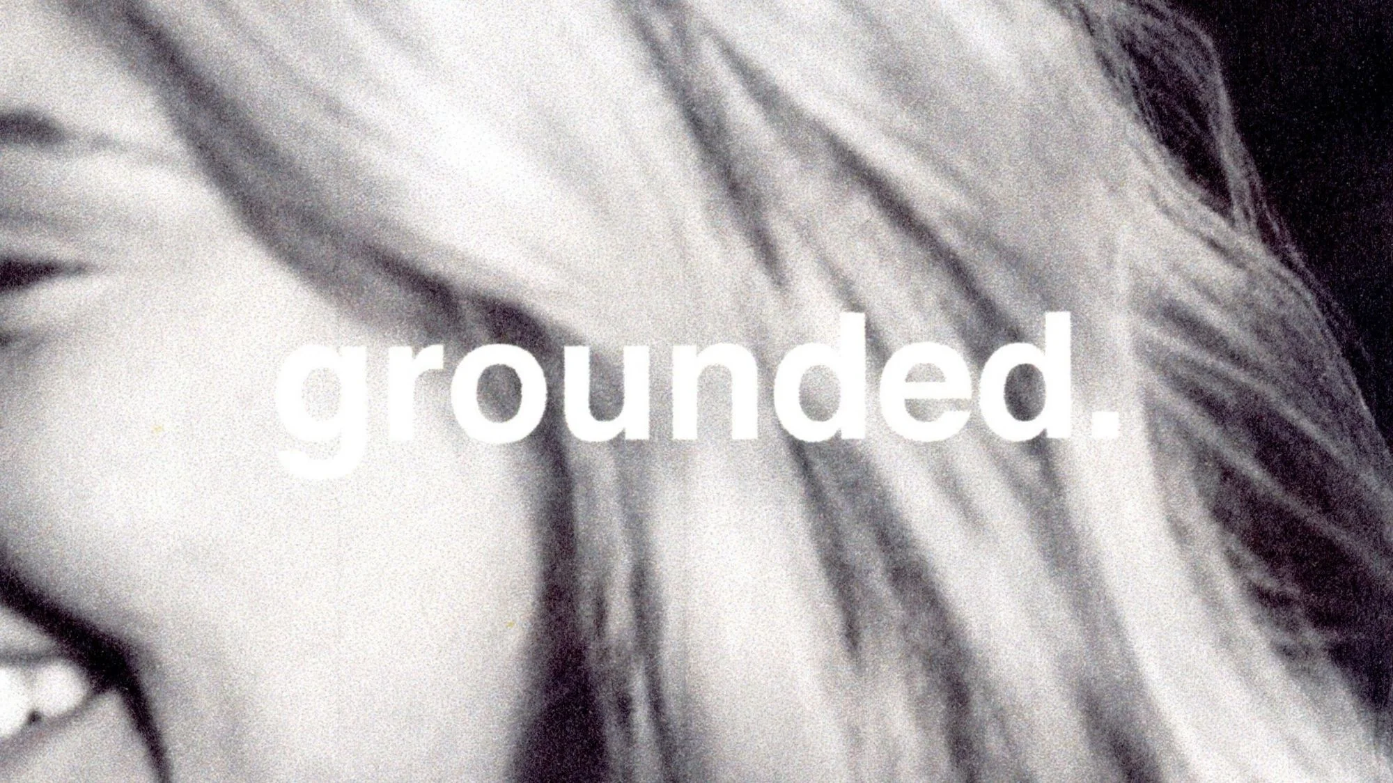 Close-up black and white image of a smiling woman with the word “grounded” overlayed, representing emotional branding and identity in fashion, featured by C2 Fashion Studio’s trend forecasting platform.