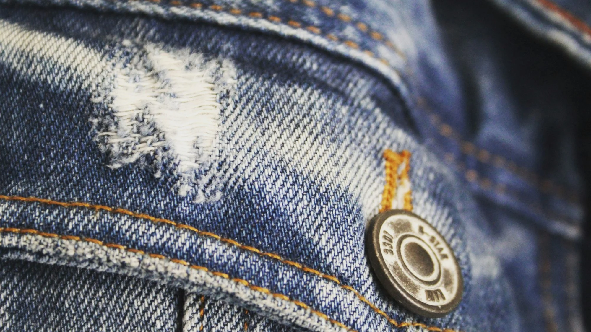 Close-up of denim fabric with visible stitching and button, symbolizing emotional durability in fashion through repair, mending, and modular tailoring. Concept curated by C2 Fashion Studio, a leading trend forecasting agency.