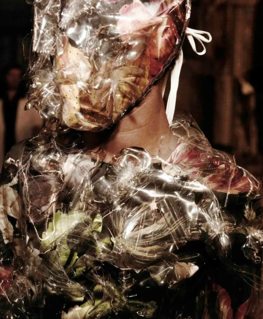 Avant-garde model in floral and plastic-textured ensemble representing Resonant Grounding, the central macro trend for Autumn Winter 2027/2028, decoded by C2 Fashion Studio’s trend forecasting platform.