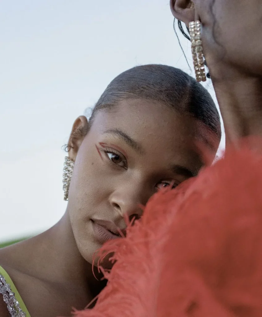 Close-up portrait of a model in elegant red feathered detail, symbolizing craftsmanship and cultural identity in a fashion trend highlighted by C2 Fashion Studio, a trend forecasting agency.