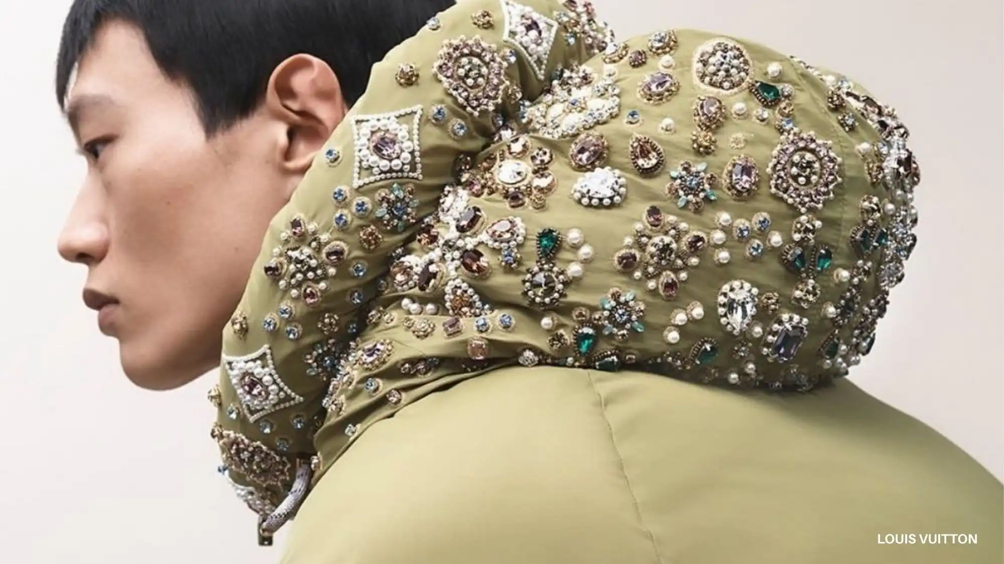 Model wearing an olive-green Louis Vuitton jacket embellished with intricate jewels and pearls, representing the Neoheritage & Flux fashion trend for Autumn Winter 2026–2027 that fuses traditional craftsmanship with digital-era innovation.