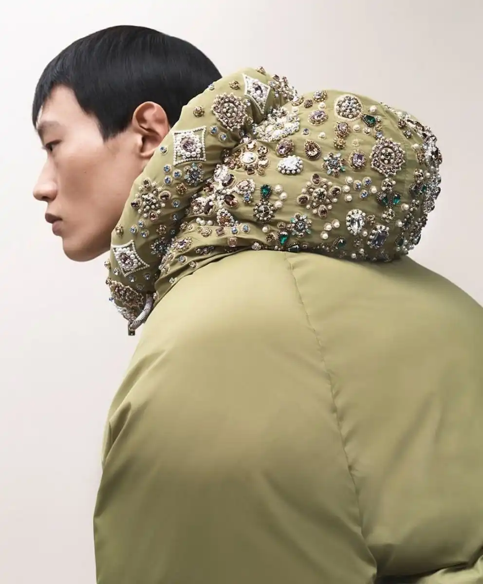 Close-up of a model wearing an olive green jacket richly embroidered with jewels and pearls, symbolizing the Neoheritage & Flux fashion trend merging craft and digital innovation for Autumn Winter 2026–2027.