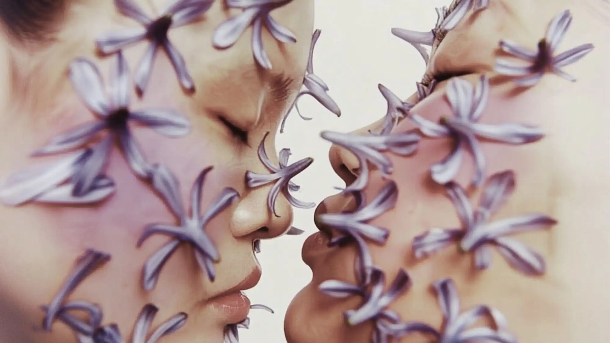 Two faces adorned with delicate purple flower petals in a soft, ethereal composition, symbolizing regenerative aesthetics, bio-inspired design, and sustainability trends explored by C2 Fashion Studio.