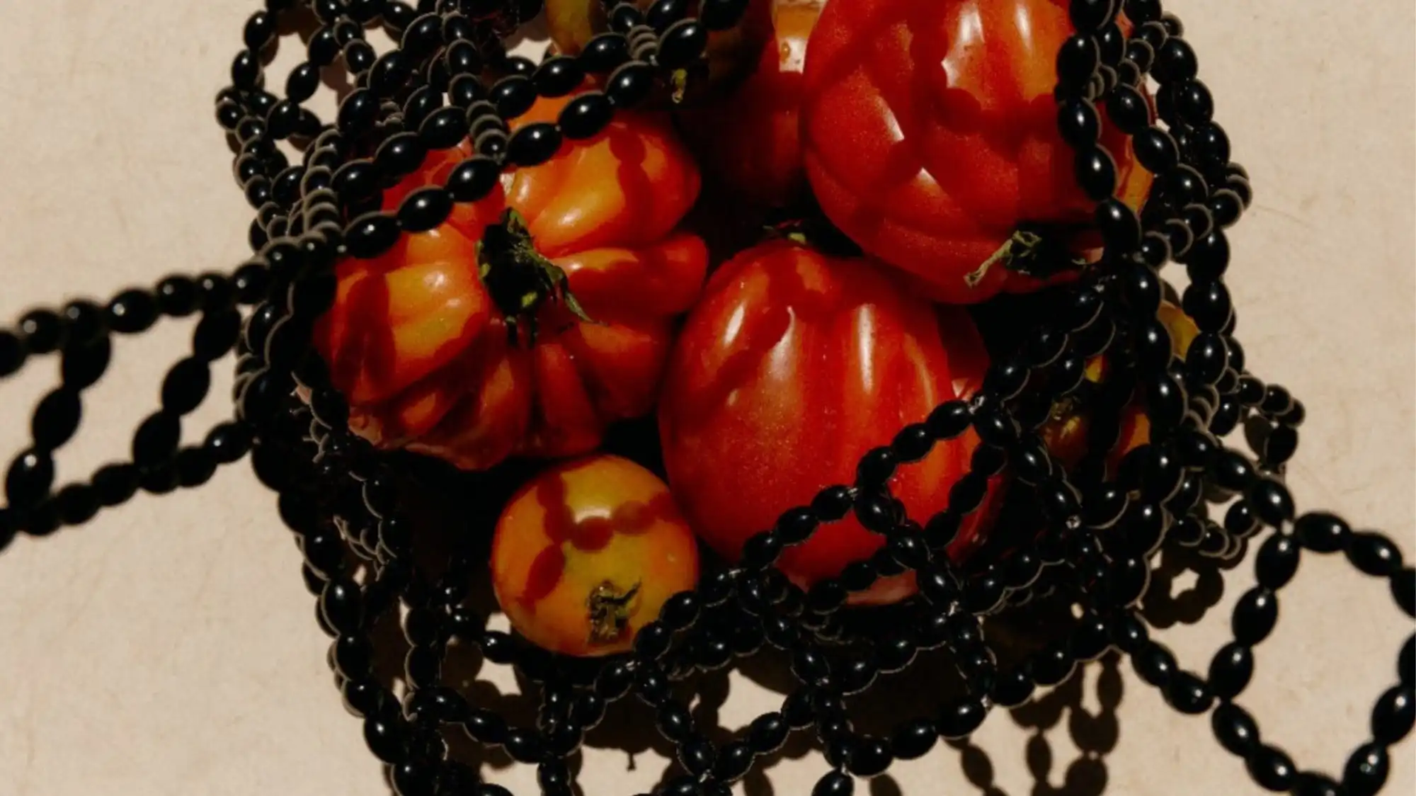 Close-up of red tomatoes intertwined with black beaded jewelry, symbolizing Conscious Vitality — the C2 Fashion Studio macro trend for Spring Summer 2027 exploring emotional intelligence, sensory connection, and mindful design in fashion.