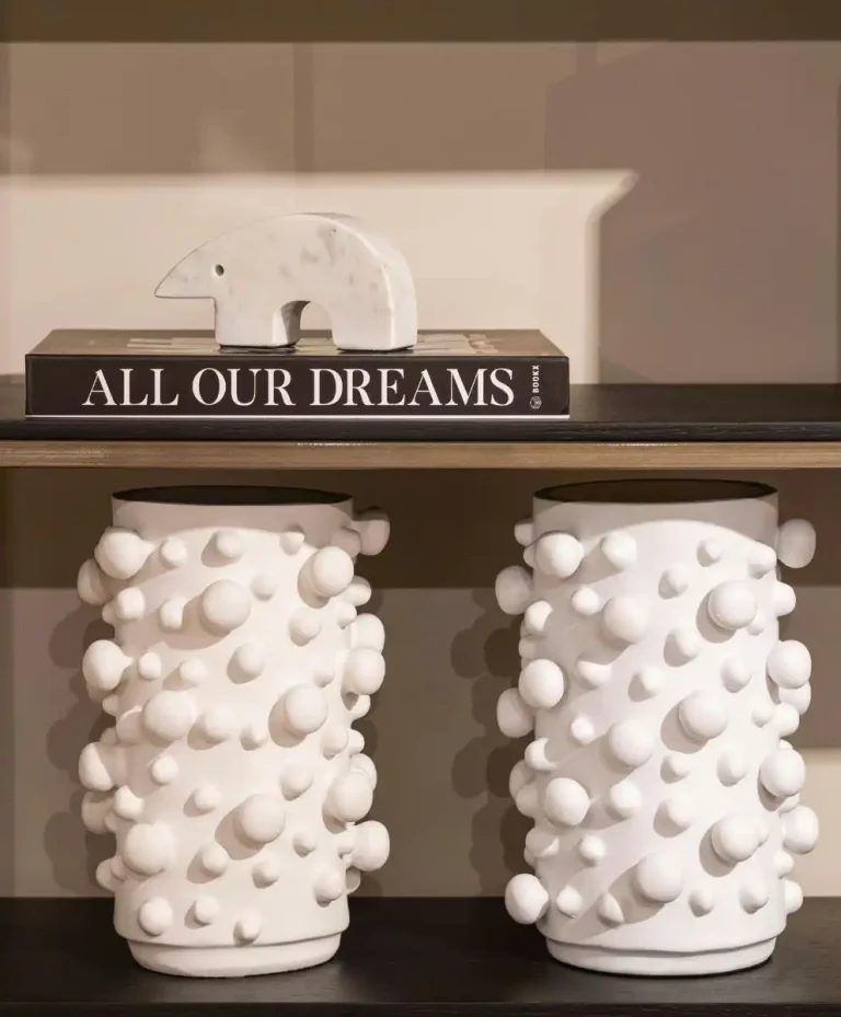White sculptural ceramic vases with rounded 3D textures displayed on a modern shelf with a marble bear figurine and a book titled “All Our Dreams,” showcasing luxury home decor and contemporary interior design trends.