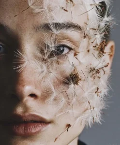 A close-up portrait of a person’s face covered in delicate dandelion seeds, symbolizing regenerative design, bio-inspired aesthetics, and sustainability trends explored by C2 Fashion Studio.