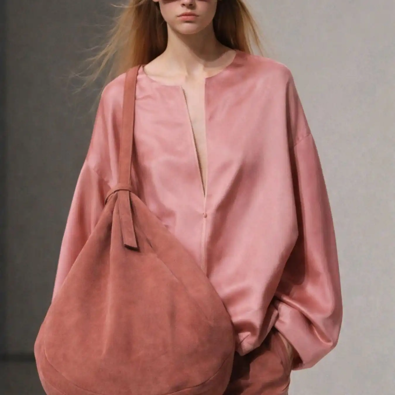 Fashion runway model wearing a silky pink oversized blouse with a large suede shoulder bag, capturing soft minimalism and relaxed luxury for Spring Summer 2028 trend forecasting.
