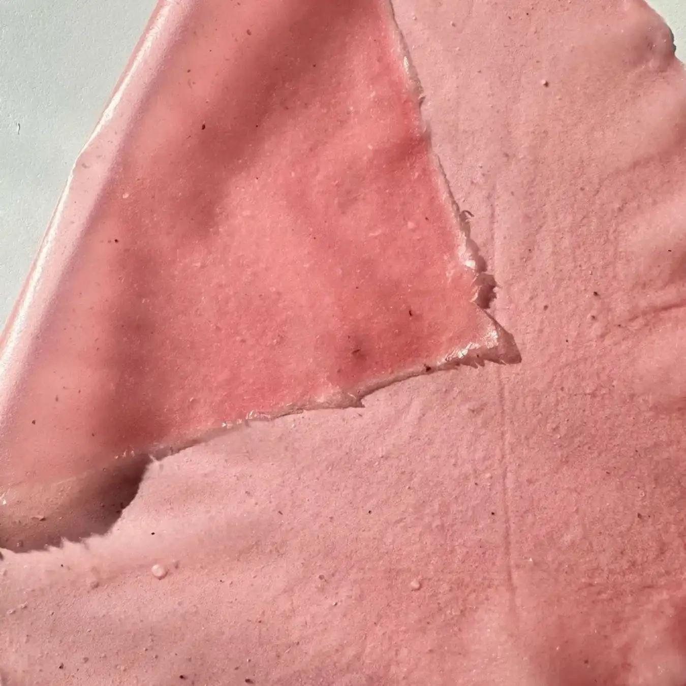 Close-up of a soft pink textured surface with layered translucent material and tiny speckles, showing tactile material innovation for Spring Summer 2028 trend forecasting.