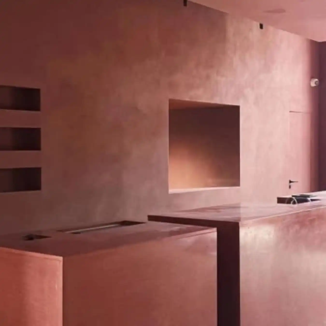 Minimalist interior with warm pink walls, built‑in niches and clean geometric counters, reflecting calm precision and architectural balance for Spring Summer 2028 trend forecasting.