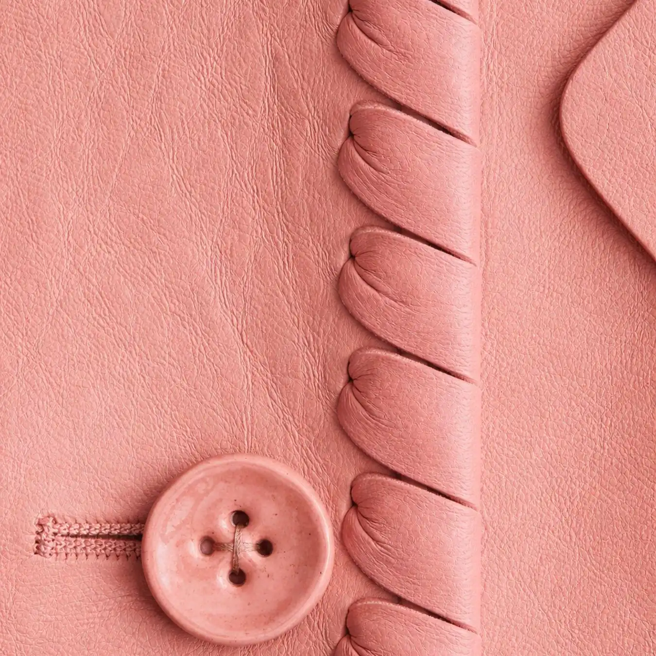 Close-up of a pink leather surface with a large button and braided seam detail, highlighting soft-touch material innovation for Spring Summer 2028 fashion trend forecasting.