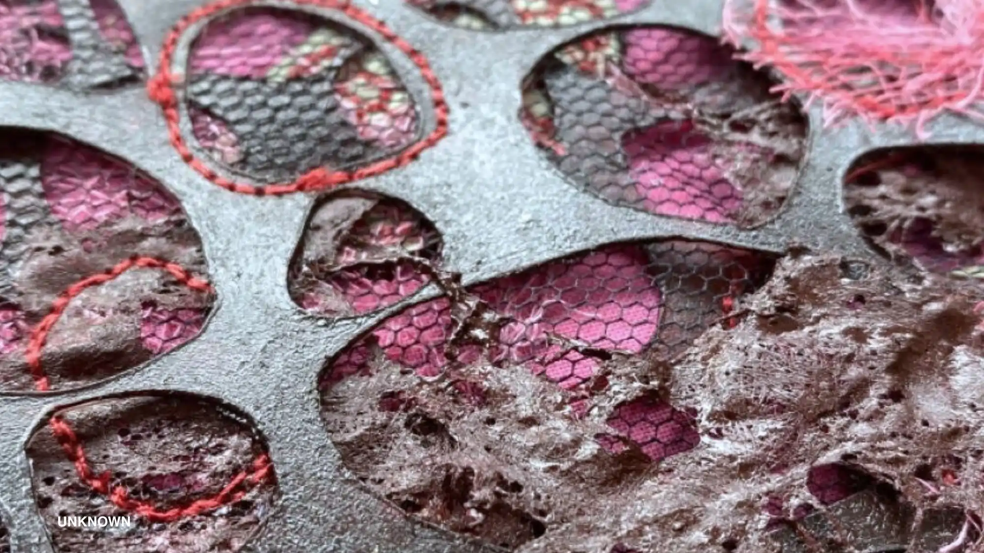 Close‑up of a perforated, decayed textile with circular cut‑outs revealing pink mesh and frayed, mould‑like fibres, illustrating dirty aesthetics and Entropism in fashion materials.