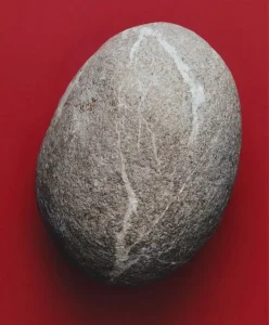 Smooth grey stone with subtle white veins placed on a bold red background, symbolising calm refinement and grounded luxury for April 2026 fashion and design trends.