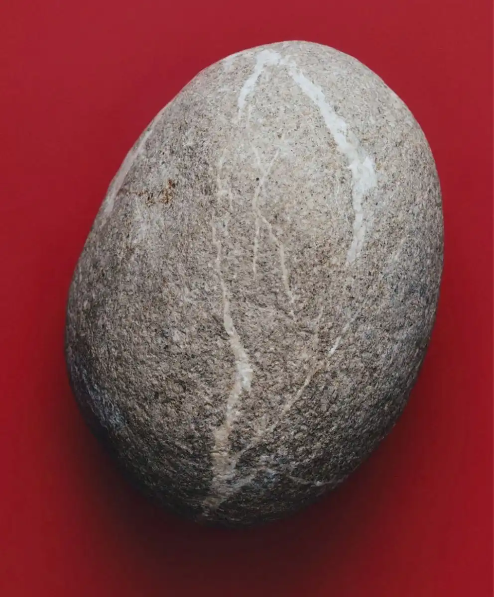 Smooth grey stone with subtle white veins placed on a bold red background, symbolising calm refinement and grounded luxury for April 2026 fashion and design trends.