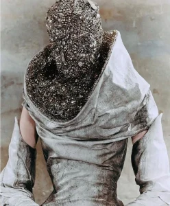 Back view of a model in a distressed silver gown with a heavily encrusted, jewel‑covered headpiece, expressing Entropism and material decay as a fashion trend.
