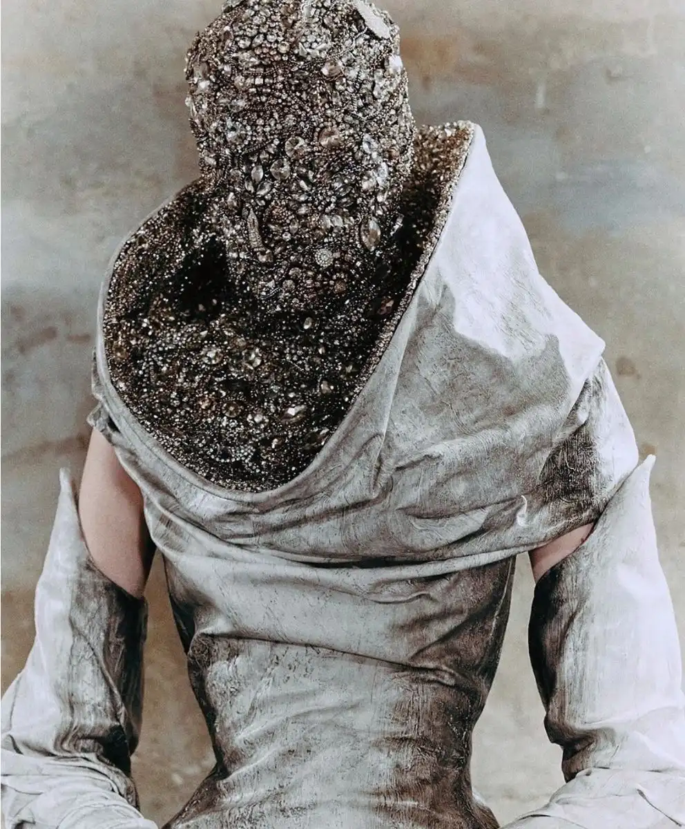 Back view of a model in a distressed silver gown with a heavily encrusted, jewel‑covered headpiece, expressing Entropism and material decay as a fashion trend.