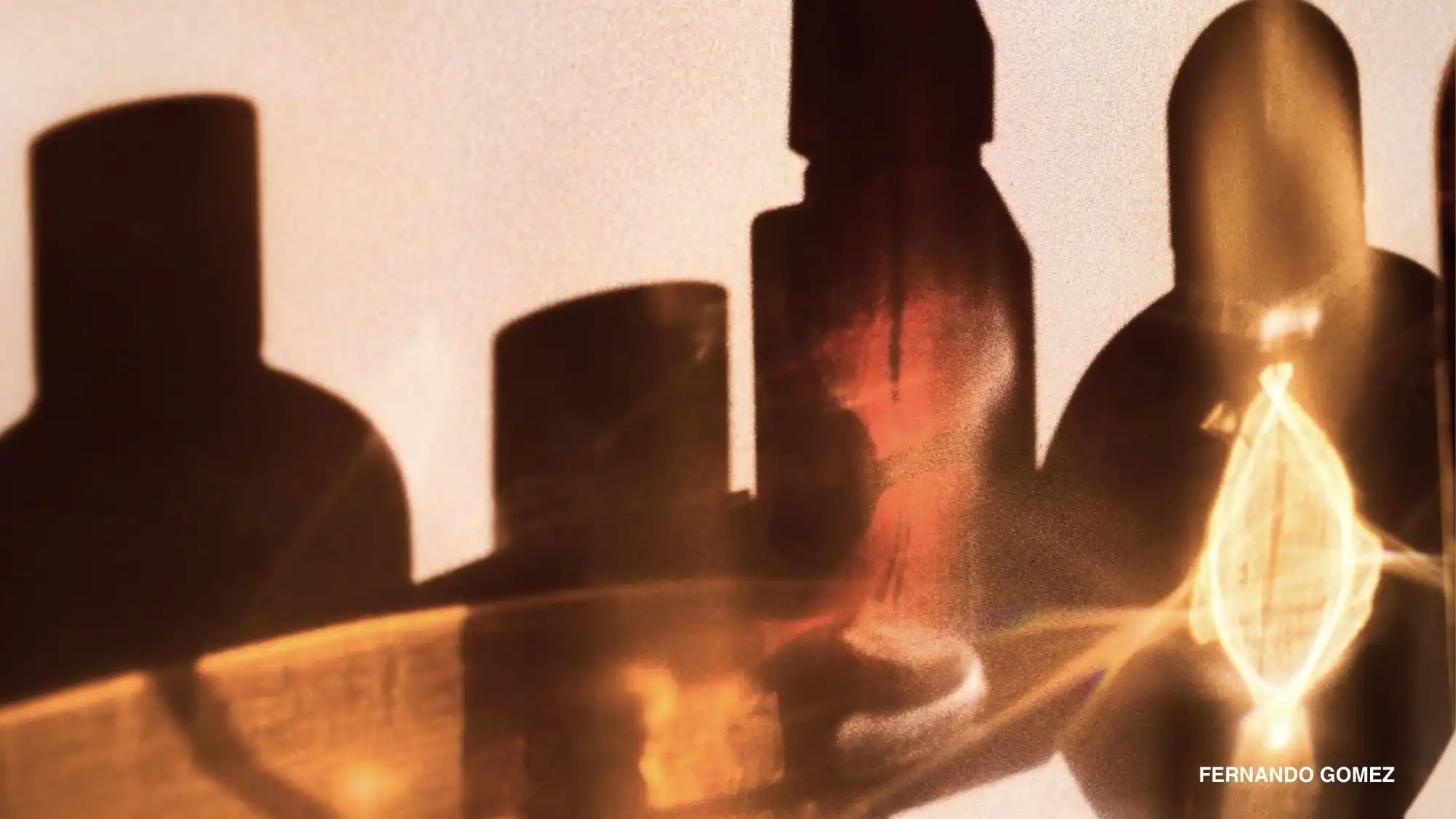 Backlit silhouettes of fragrance bottles glowing amber against a soft cream wall, illustrating sensorial comfort in C2 Fashion Studio trend forecasting.
