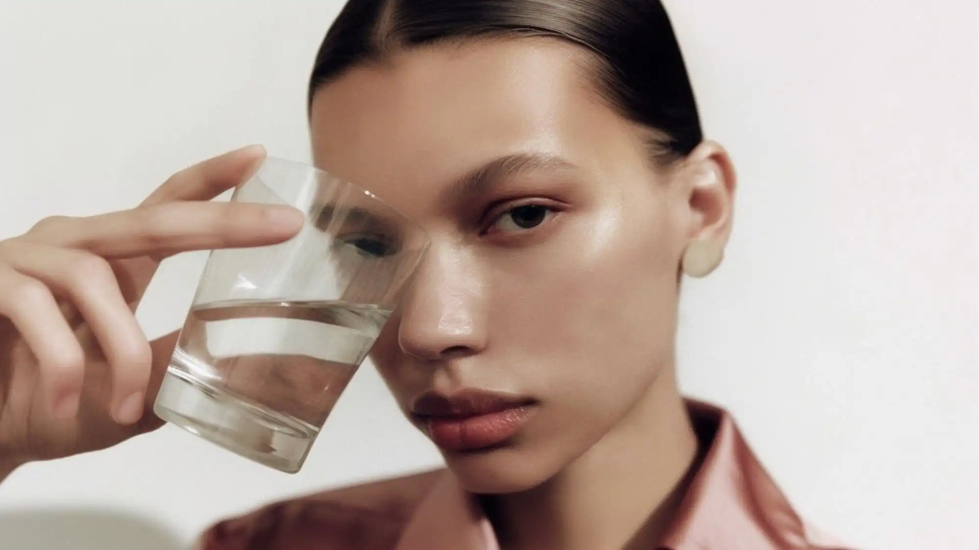 Beauty Trend Forecasting visual featuring luminous skin, natural makeup, and a model holding a glass of water, symbolizing hydration, skin longevity, wellness innovation, and evolving consumer priorities in beauty and self-care.