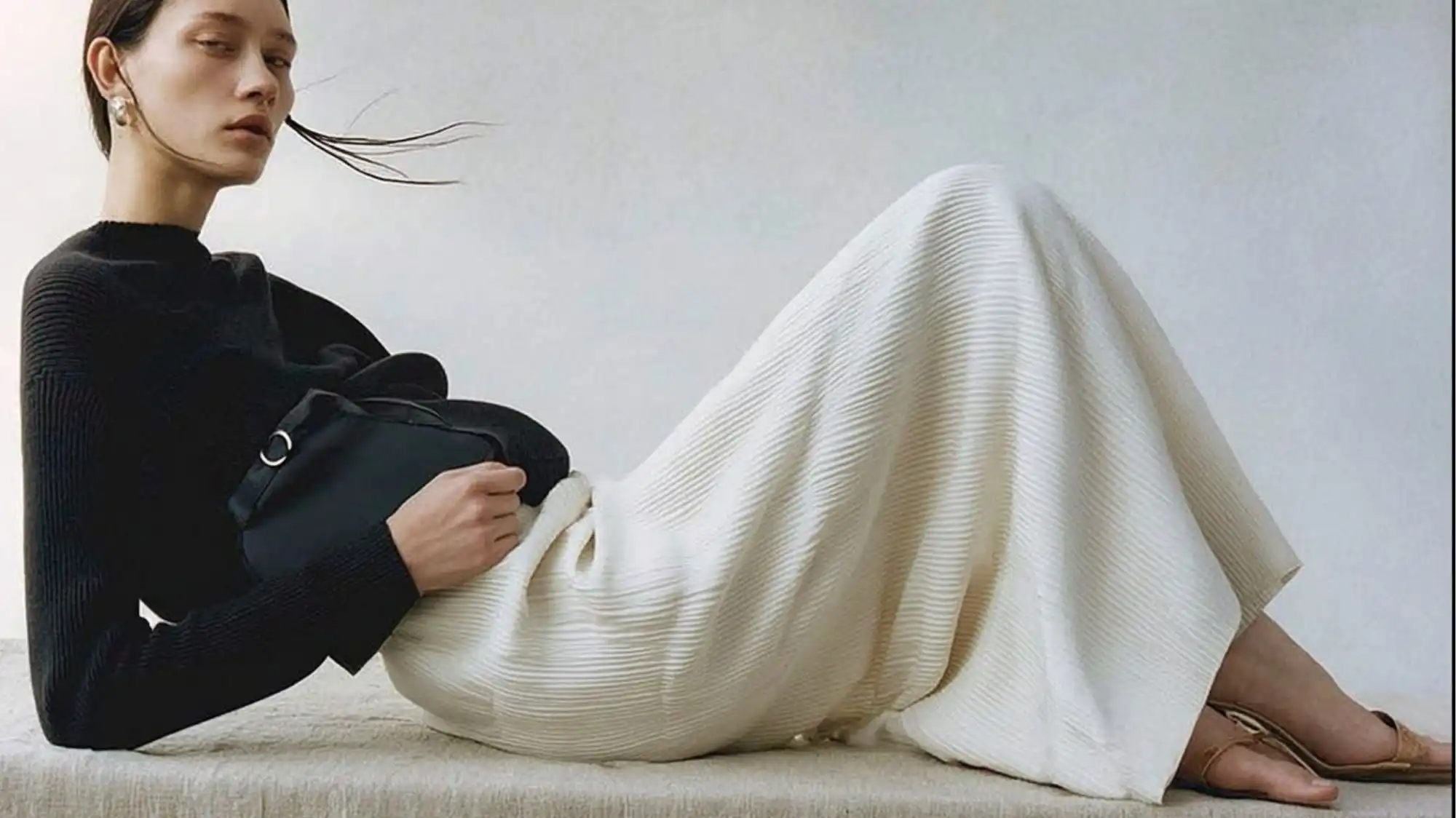 Fashion Trend Forecasting image featuring a minimalist black-and-ivory ensemble with fluid pleated textures, refined accessories, and understated luxury, reflecting contemporary elegance, emotional durability, and timeless wardrobe design.