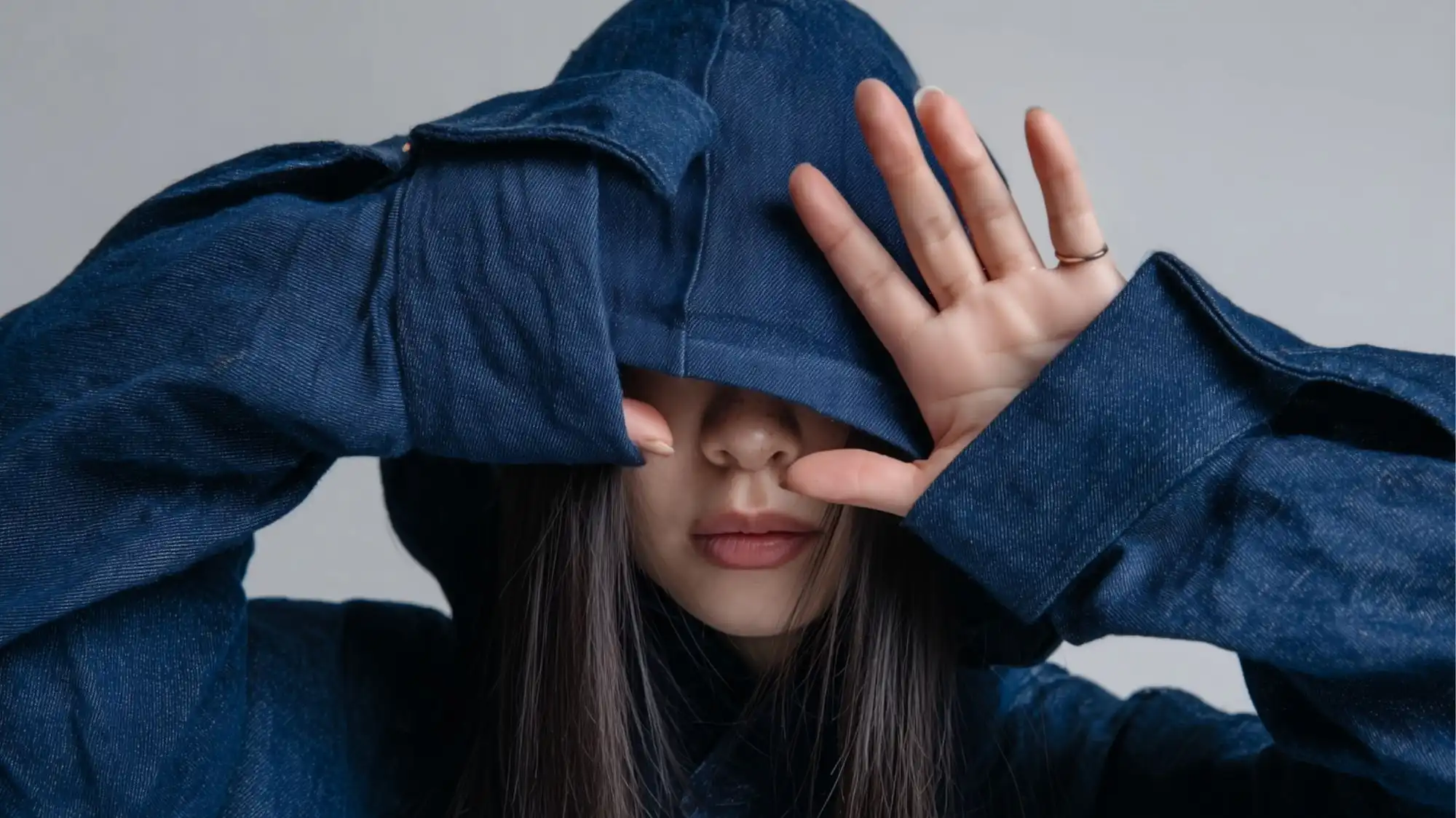 Circularity 2026 fashion trend forecasting image featuring a model wearing an oversized indigo denim garment with extended sleeves and protective hood styling. The look reflects durability, timeless materials, product longevity, repairability, and circular fashion design focused on maximizing material lifespan.