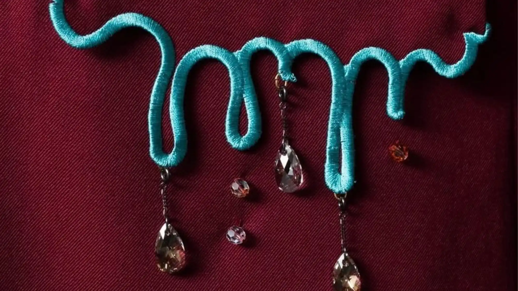 Abstract embroidered textile artwork with flowing turquoise forms and crystal embellishments, representing Transformative Narrative Design, expressive craftsmanship, and emotional storytelling in Fashion Trend Forecasting by C2 Fashion Studio.