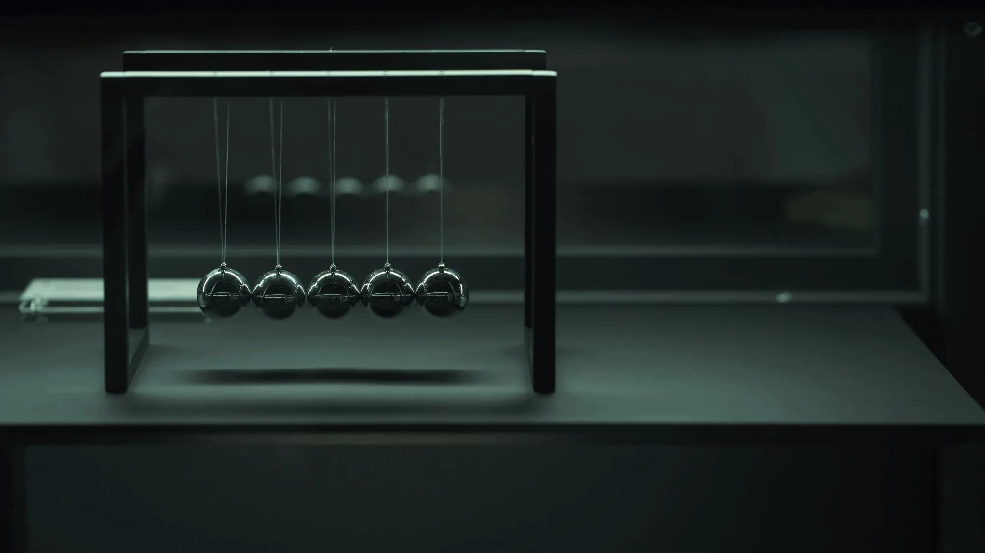 Autumn Winter 2028 2029 color trends by C2 Fashion Studio, featuring a metallic Newton’s cradle against a dark green architectural background, reflecting technological precision and Human Equilibrium.